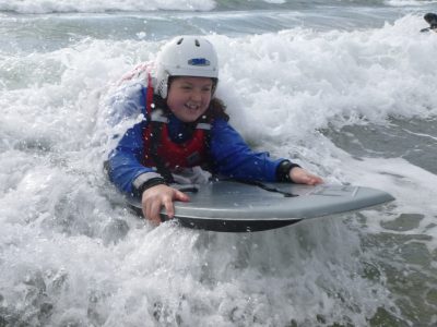 A school student rides a wave towards the beach with a smile on her face.
