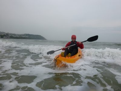 A school student surfs a wave on a open top kayak.